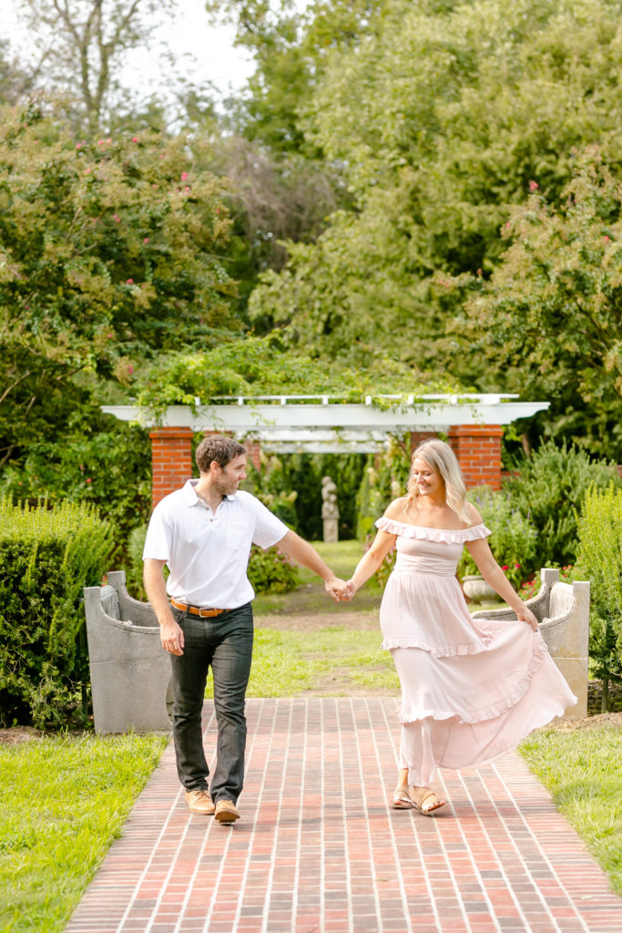 girl in pink swinging dress as her and guy walk through garden