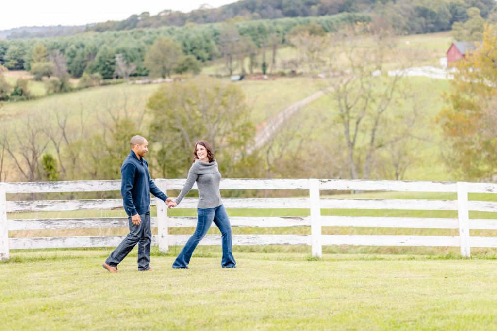 couple walking hand in hand, girl leading in front, with rolling hills and fence line behind them