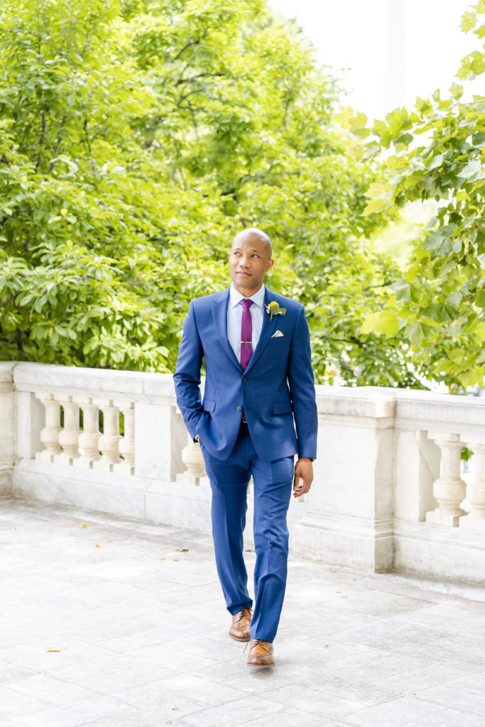 groom walking in blue suit and purple tie