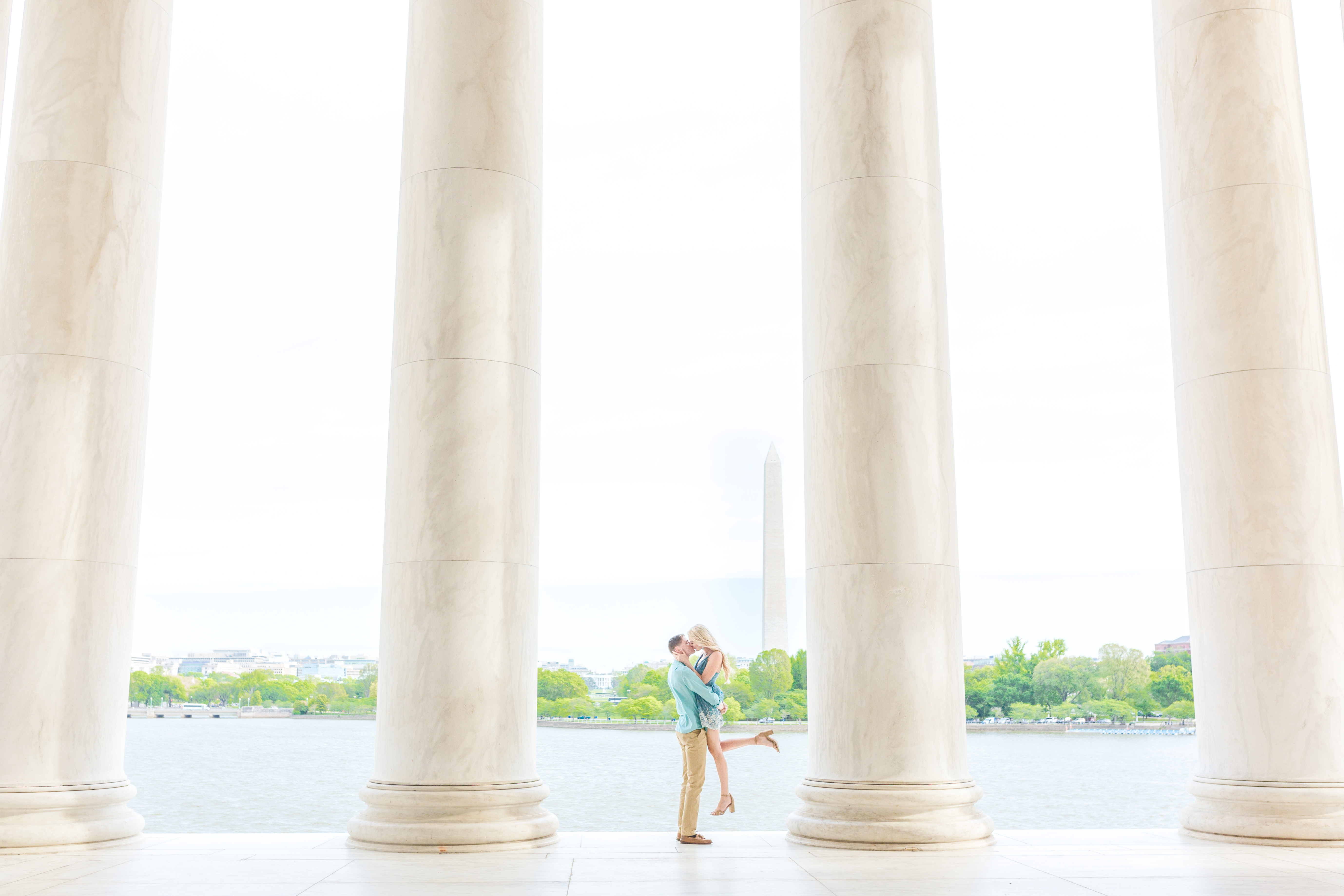 couple kissing in jefferson memorial columns with Washington Monument in background, boy lifting girl off ground