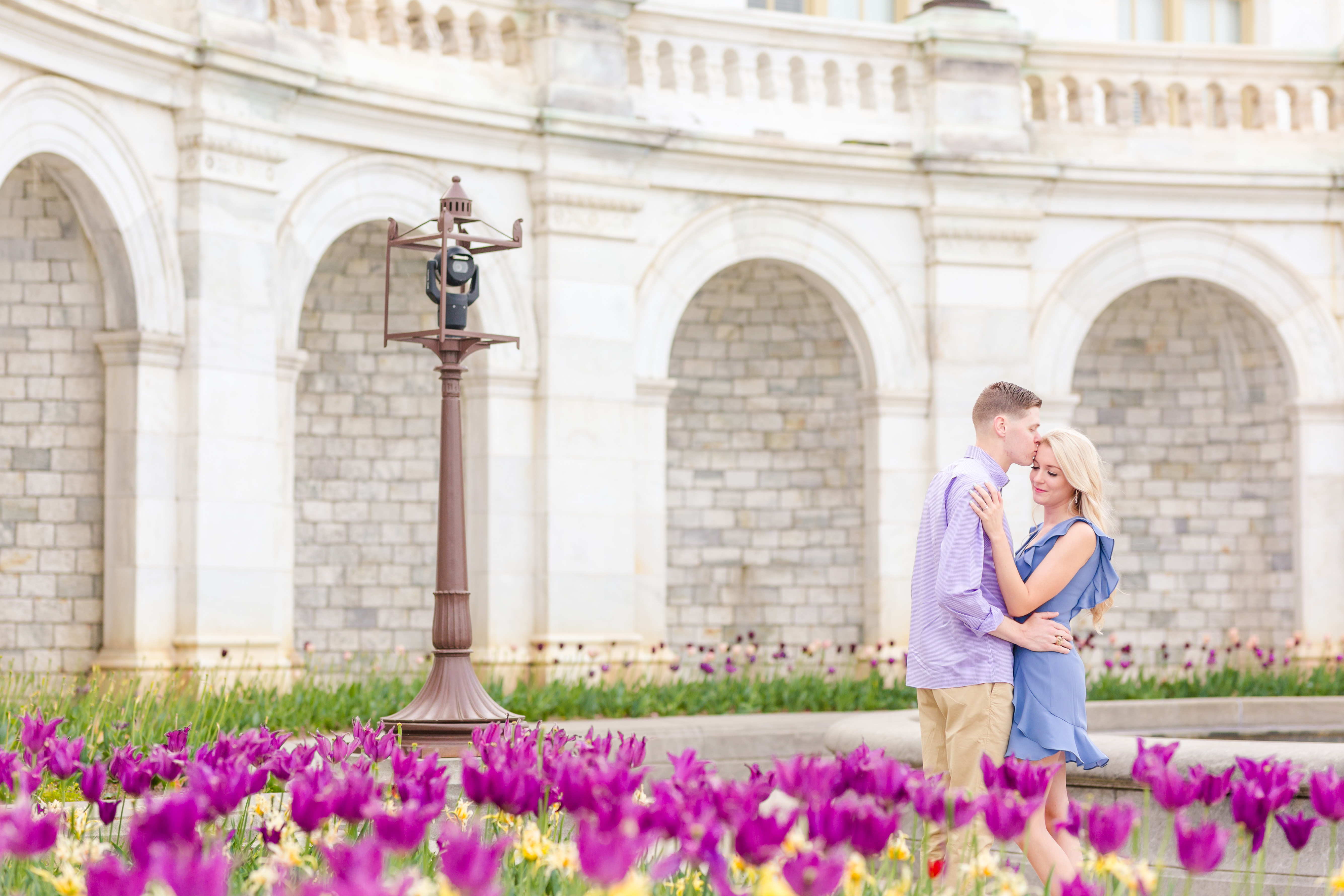 couple facing eachother, guy kissing girl on forehead in front of capitol with tulips in foreground 