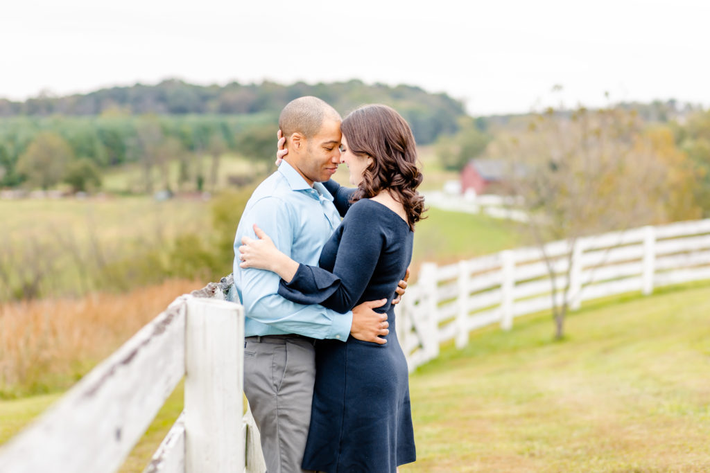 couple embracing on fence over looking rolling hills 
