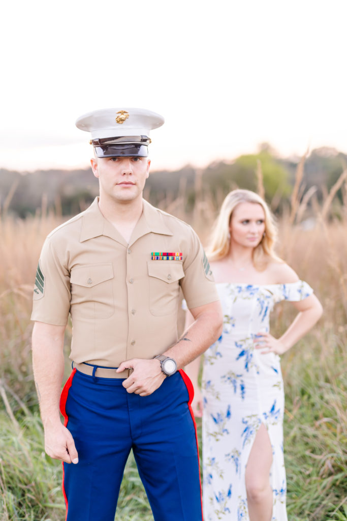 Couple standing in open field with tall grass. Guy in Marines uniform, girl in white and blue floral dress