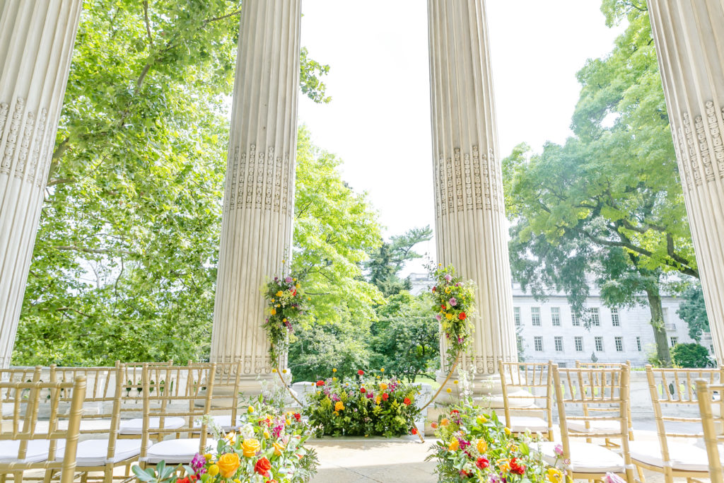 Colorful garden aisle leading to half circle arch in front of tall columns of DAR