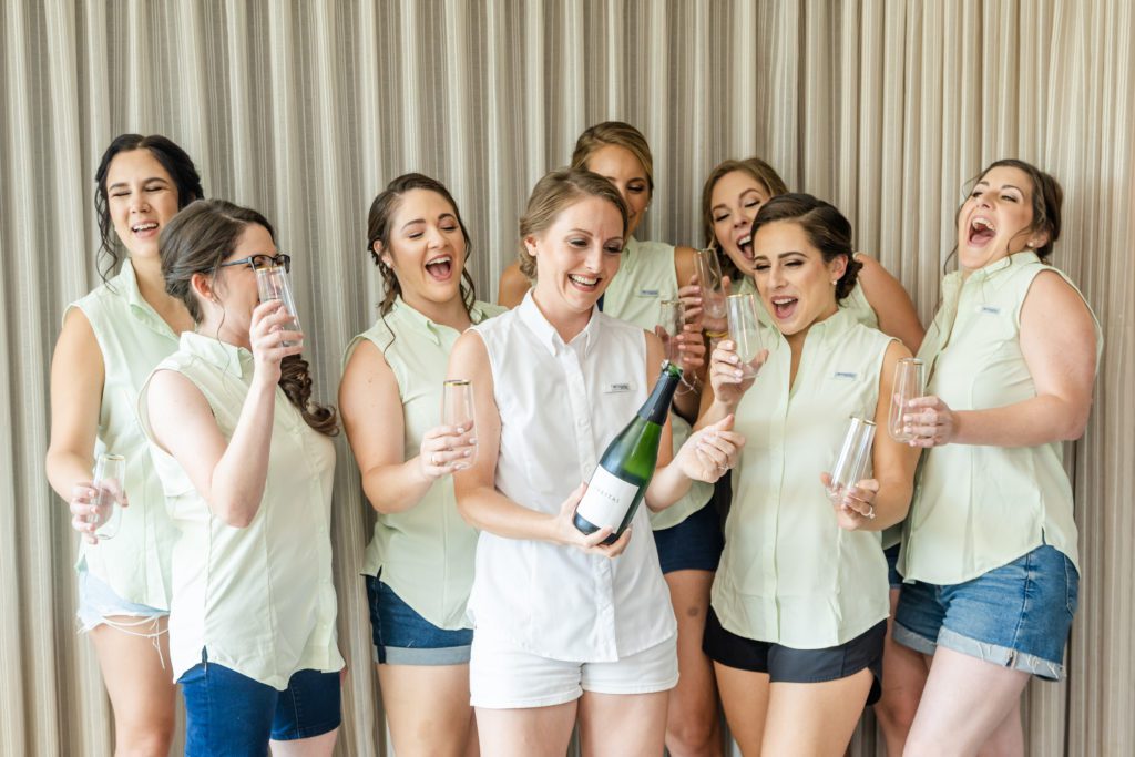 bride with her bridesmaids popping a bottle of champagne 